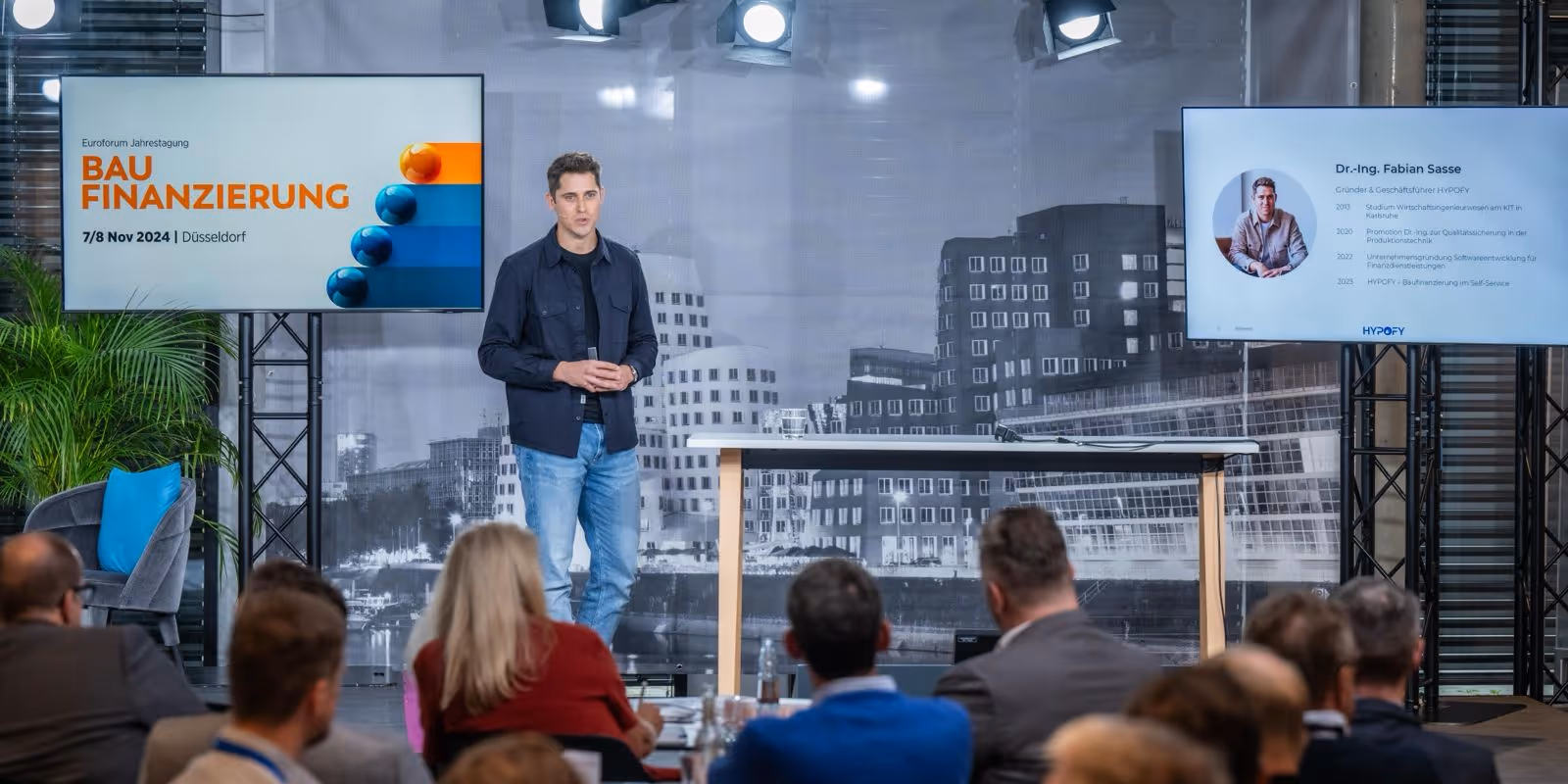 Dr. Fabian Sasse, der Gründer und Geschäftsführer von HYPOFY auf der Bühne vor ca. 20 Zuschauern aus der Baufinanzierungs-Branche. Die Präsentation zeigt eine Folie mit der Überschrift: Baufinanzierung.